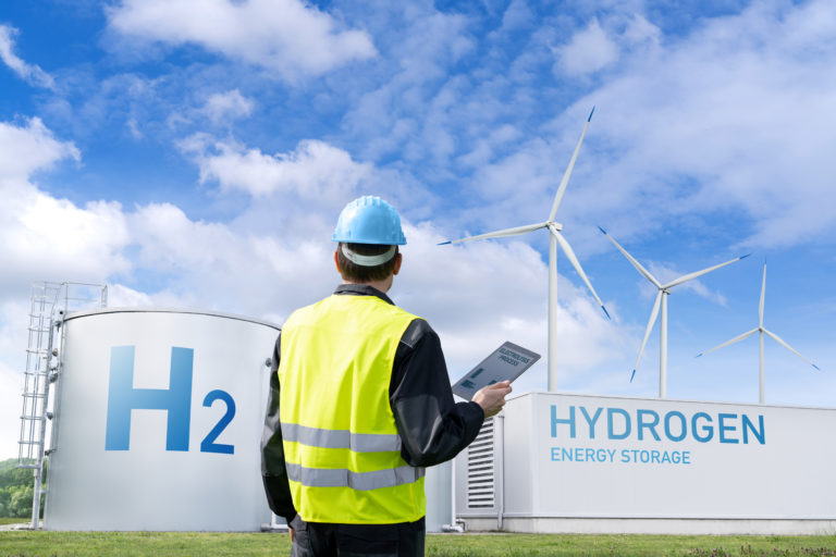 Bureau Veritas auditor overseeing a renewable hydrogen production and storage facility, featuring H2 tanks and wind turbines, in compliance with CertifHy EU RFNBO Voluntary Scheme.